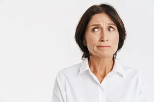 Mulher com expressão preocupada, vestindo camisa branca, olhando para o lado, transmitindo desconforto e incerteza, ideal para ilustrar emoções e estresse.