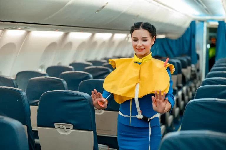 Empresária de aviação no interior de um avião, com uniforme azul e colete de salva-vidas amarelo, demonstrando segurança e atendimento em voo.