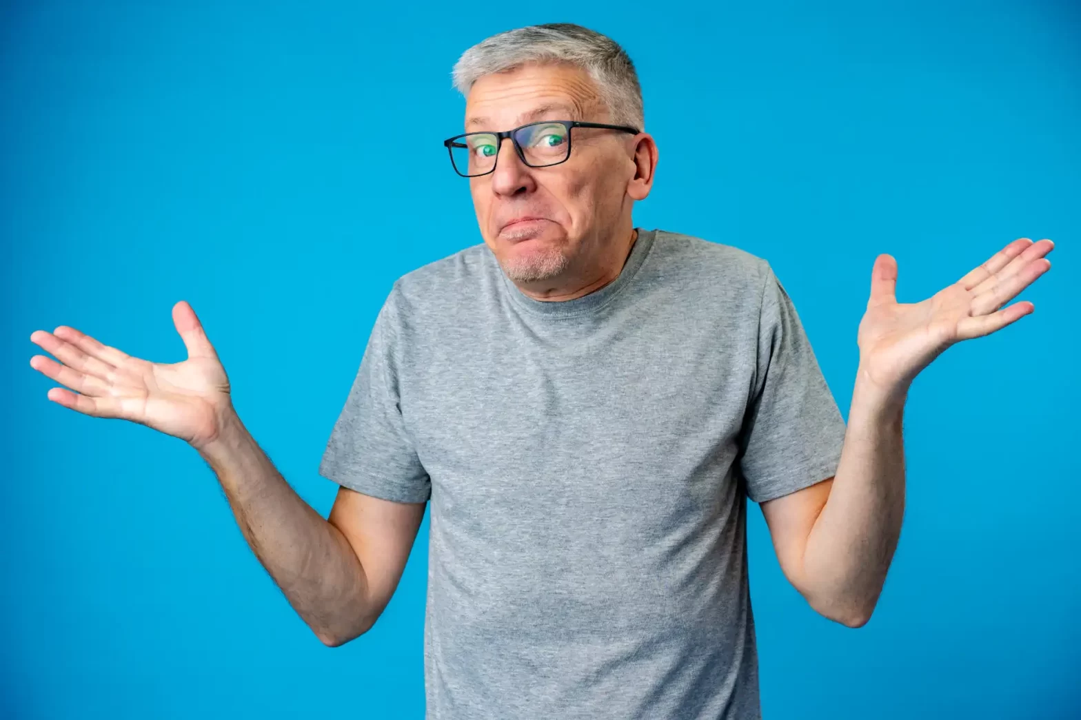 Homem com expressão de dúvida, vestindo camiseta cinza e óculos, com cabelo cinza claro, gesticulando com as mãos de forma incerta contra fundo azul. Tipos de Aposentadoria no Brasil.
