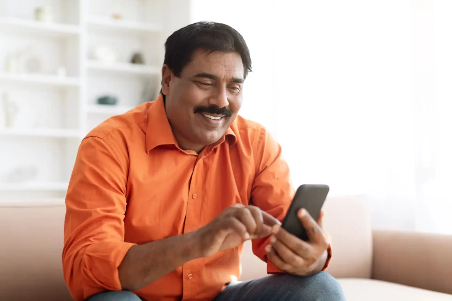 Homem sorridente usando smartphone em ambiente aconchegante, expressão de felicidade, lazer ou comunicação digital, ideal para temas relacionados a tecnologia e conexão. Ferramentas para Planejamento Previdenciário.