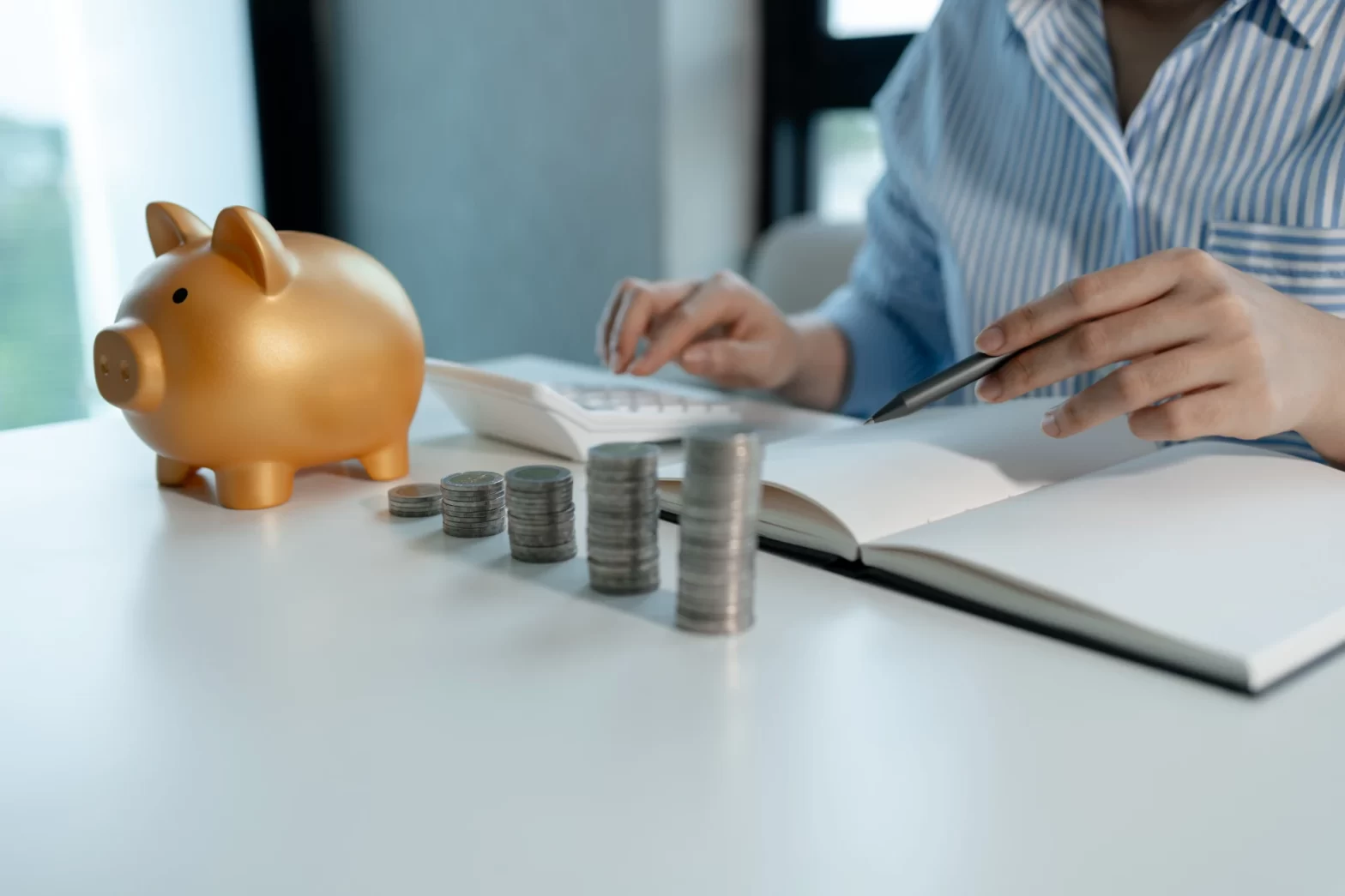 Pessoa planejando economia financeira com uma porca de piggy bank, moedas empilhadas e uma calculadora em uma mesa de escritório. Investimentos Complementares para Aposentadoria.