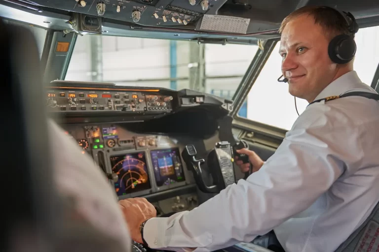 Piloto de avião sorrindo na cabine, controlando a aeronave com fones de ouvido, em ambiente de cockpit com instrumentos de voo. Post sobre saúde mental dos aeronautas.