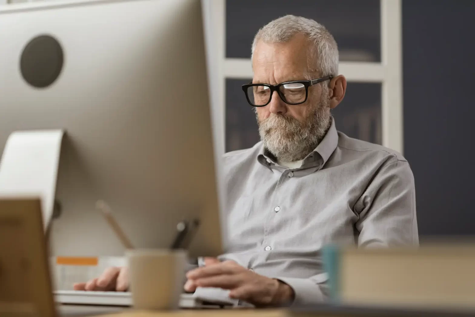 Homem de meia idade, de cabelos brancos sentado em frente ao computador. Blogpost como a tecnologia pode ajudar no planejamento previdenciário.
