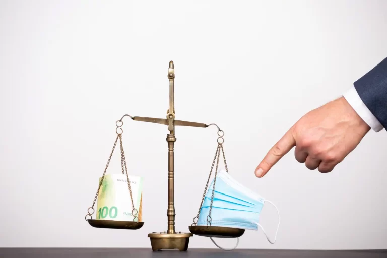 Holding Patrimonial e ITCMD. Balança antiga com uma pilha de dinheiro de um lado e máscaras faciais do outro, simbolizando o equilíbrio entre economia e saúde durante a pandemia.