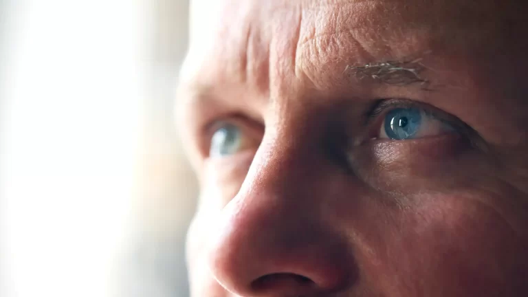 Close-up da face de um homem com olhos azuis intensos, expressão pensativa e detalhes de pele visíveis, transmitindo reflexão e foco. Post previsões para a Previdência Social no Brasil