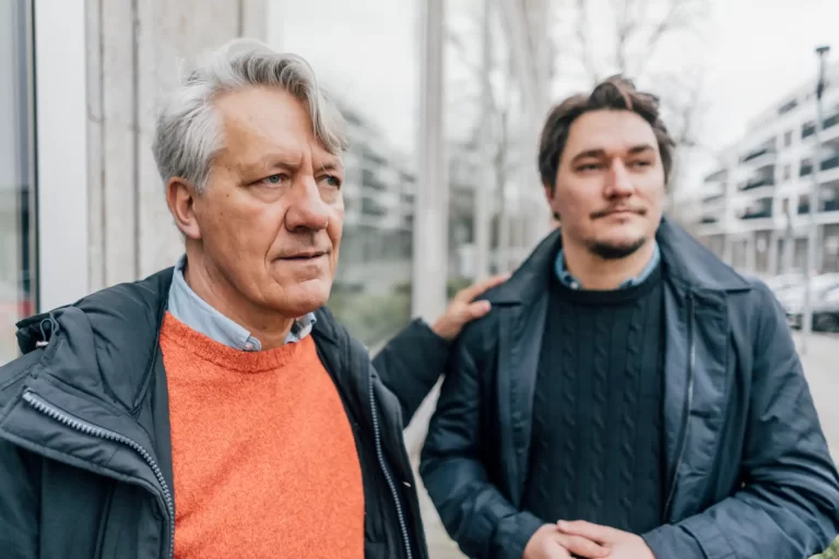 Imunidade ITBI STF. Homem mais velho com cabelo grisalho e jovem homem com cabelo escuro, ambos usando jaquetas passando por uma rua urbana, refletindo uma conversa significativa.