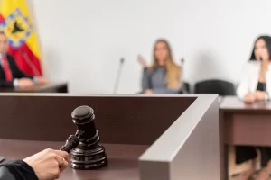 Imunidade do ITBI. Imagem de uma sala de tribunal com um martelo de juiz na mesa de julgamento e pessoas ao fundo, incluindo uma mulher com expressão séria e pessoas em debate.