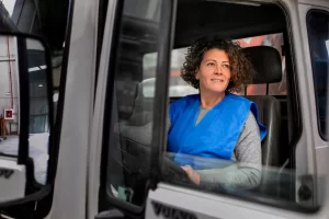 Negativa da aposentadoria especial do caminhoneiro. Mulher sorridente ao volante de caminhão, usando colete azul, representando trabalho de motorista profissional.