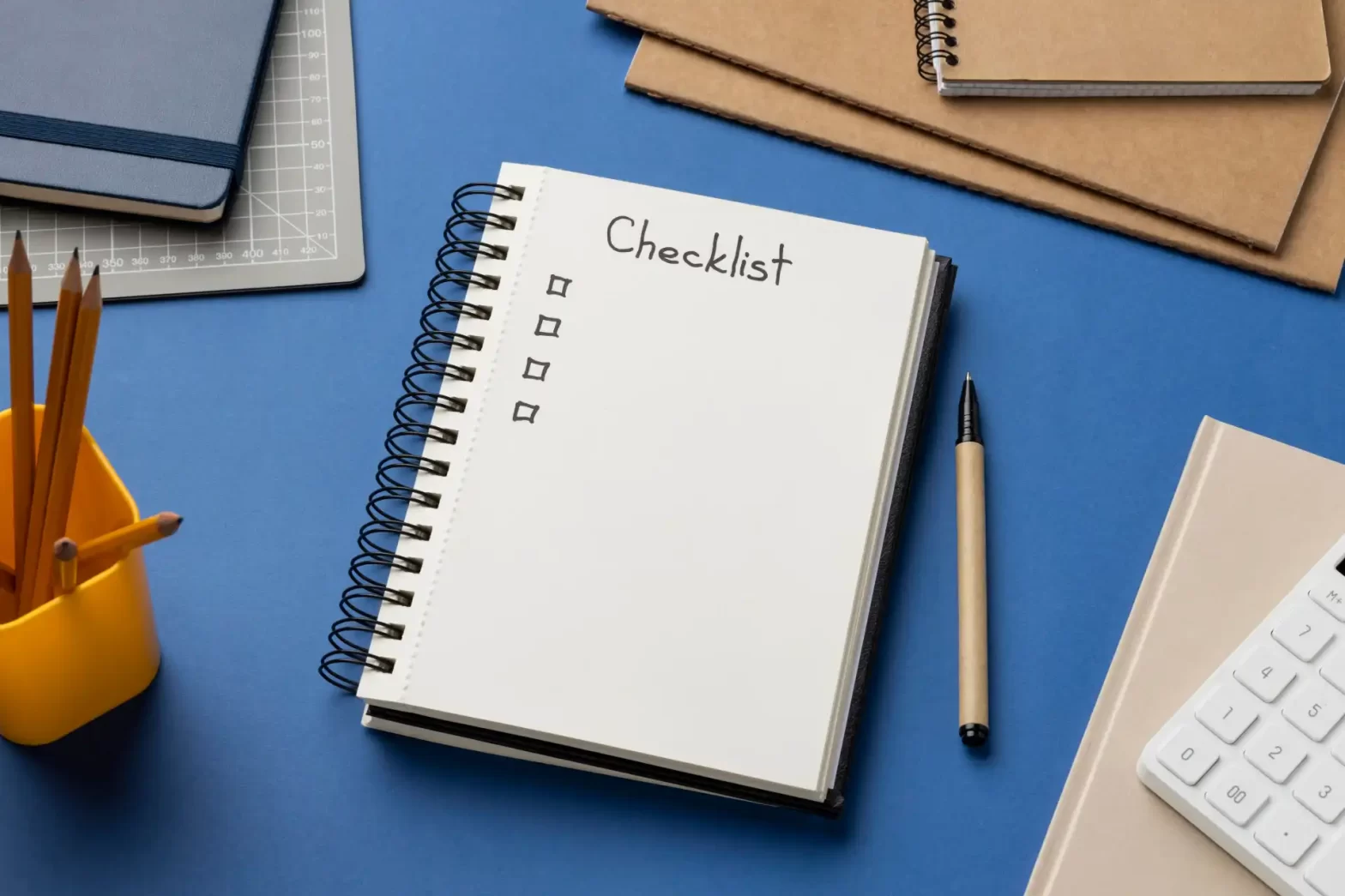 Imagem de uma mesa de escritório com uma agenda aberta com a palavra 'Checklist', canetas, cadernos e materiais de escritório para organização e produtividade.