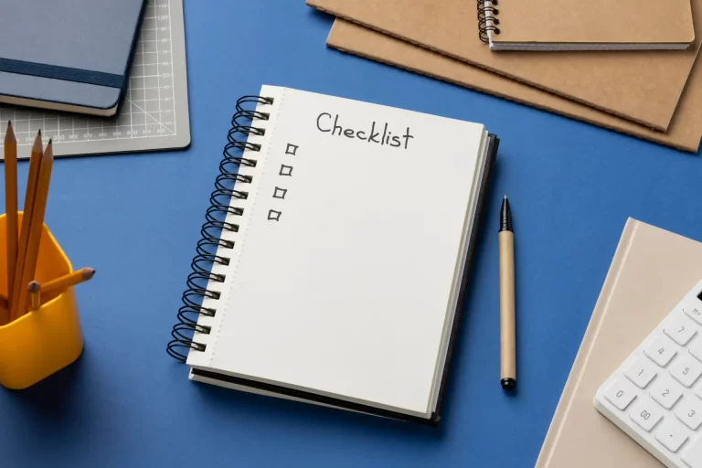 Imagem de uma mesa de escritório com uma agenda aberta com a palavra 'Checklist', canetas, cadernos e materiais de escritório para organização e produtividade.