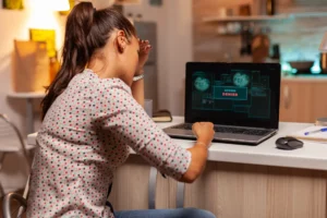 Menina trabalhando em um notebook em casa, com mensagem de “Access Denied” na tela, digitando ou treinando tarefas no computador em ambiente iluminado. Vazamento de dados.