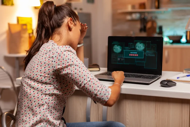 Menina trabalhando em um notebook em casa, com mensagem de “Access Denied” na tela, digitando ou treinando tarefas no computador em ambiente iluminado. Vazamento de dados.