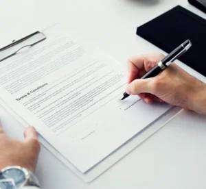 Pessoa preenchendo e assinando um documento de termos e condições em uma mesa de escritório, com caneta e folha com texto legível. Teoria do Inadimplemento Substancial: Conceito, Requisitos e Jurisprudência
